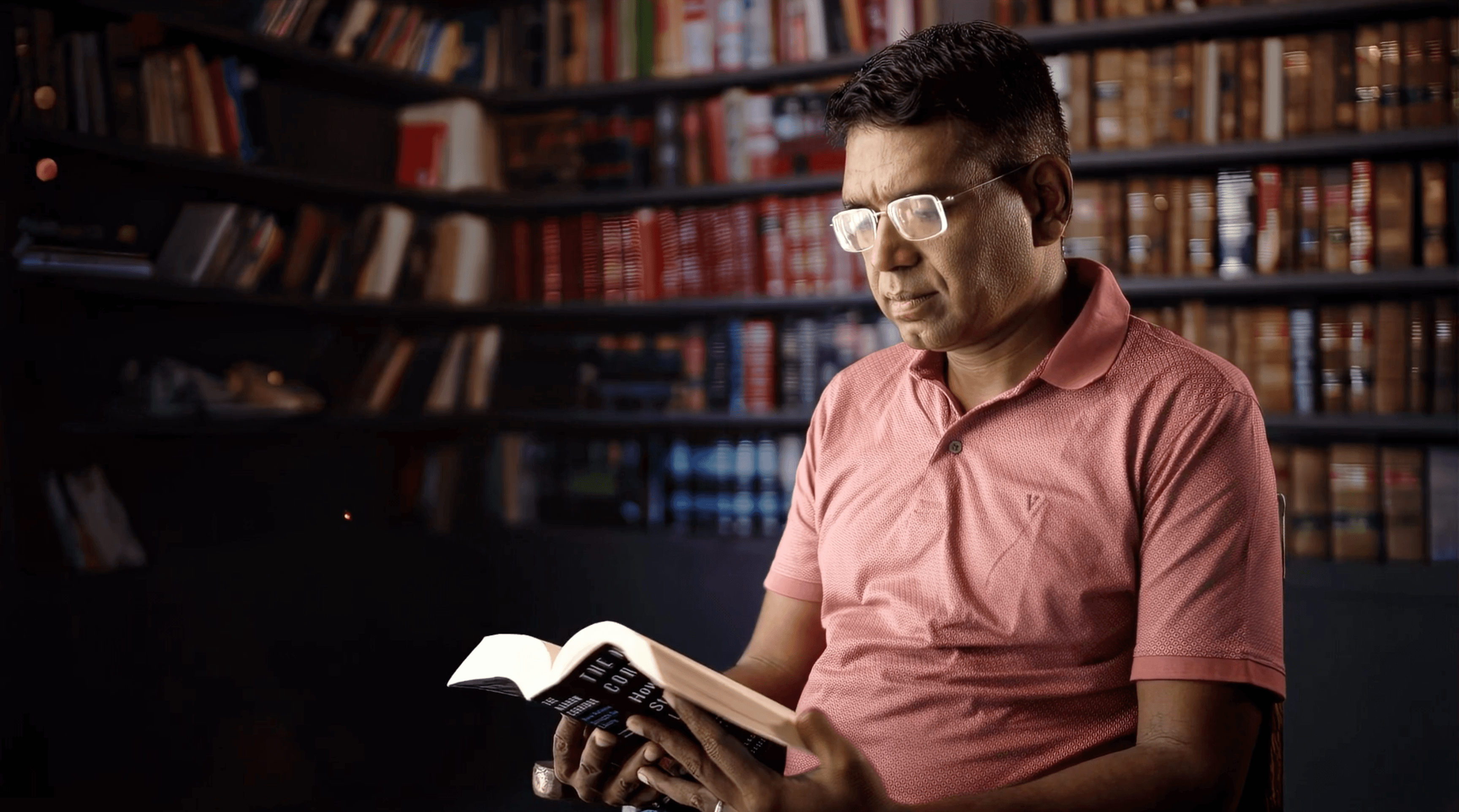 Dinesh Victor reading a book in front of a wall of bookshelves