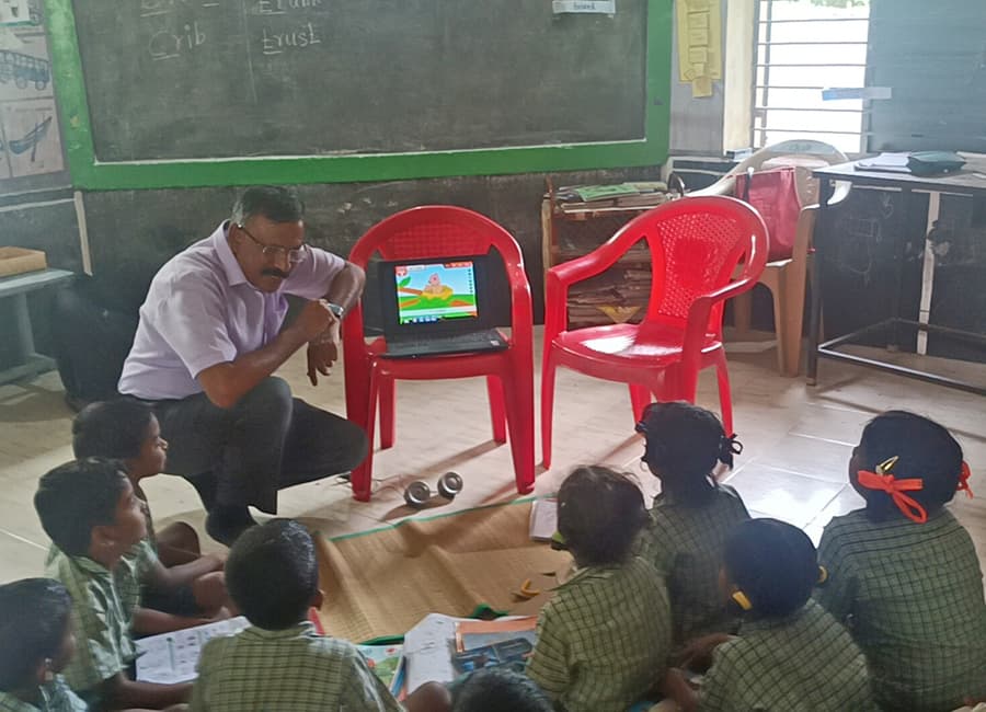 Teacher showing a lesson on a laptop to children seated on the floor