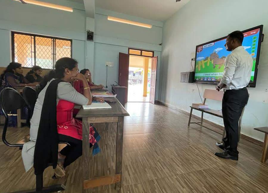 Trainer presenting at a large screen to a teacher at a desk
