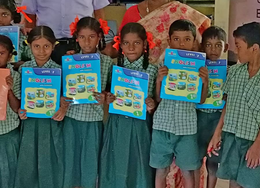 Schoolchildren in uniform smiling and holding up their MiKids English books