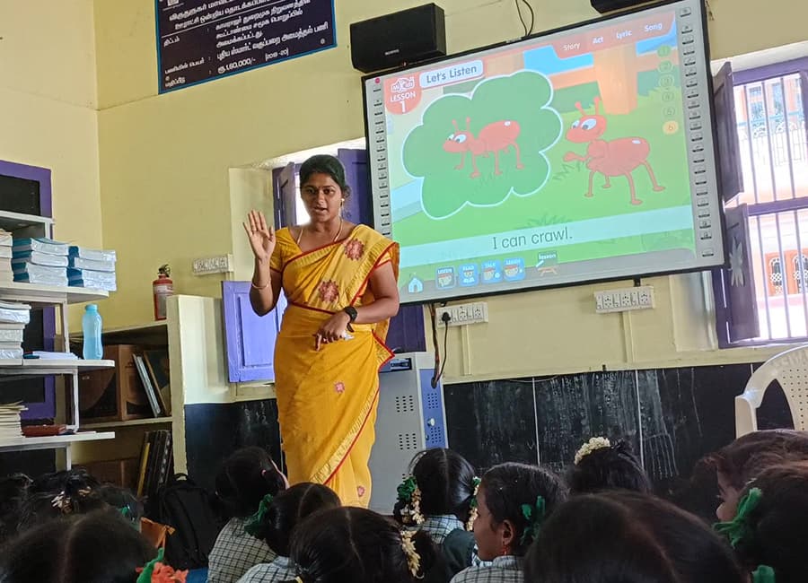 Teacher in a classroom beside a screen showing the language software